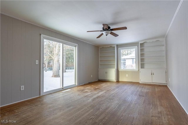 empty room with hardwood / wood-style flooring, ceiling fan, built in shelves, and ornamental molding