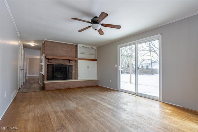 unfurnished living room featuring ceiling fan, ornamental molding, a brick fireplace, light hardwood / wood-style flooring, and built in shelves