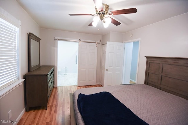 bedroom with light wood-type flooring, ceiling fan, connected bathroom, and a barn door