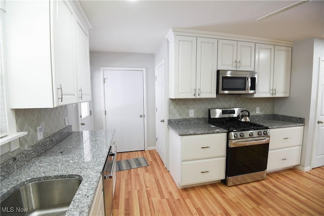 kitchen with appliances with stainless steel finishes, dark stone countertops, light hardwood / wood-style flooring, and white cabinetry