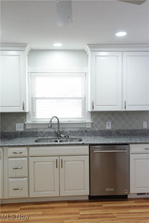 kitchen featuring decorative backsplash, dark stone counters, stainless steel dishwasher, white cabinets, and sink