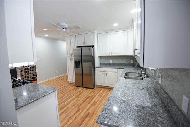 kitchen featuring white cabinetry, stainless steel fridge, decorative backsplash, light wood-type flooring, and dark stone counters