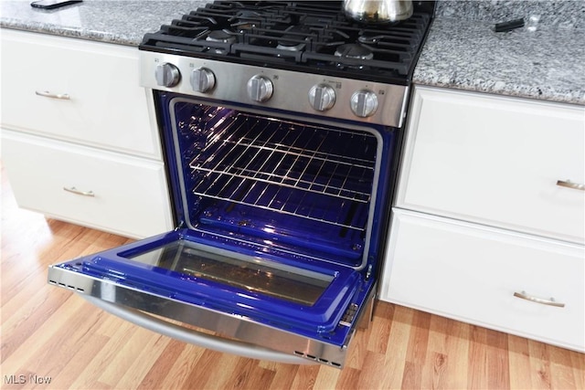 room details with light stone countertops, white cabinets, stainless steel gas range oven, and light hardwood / wood-style flooring