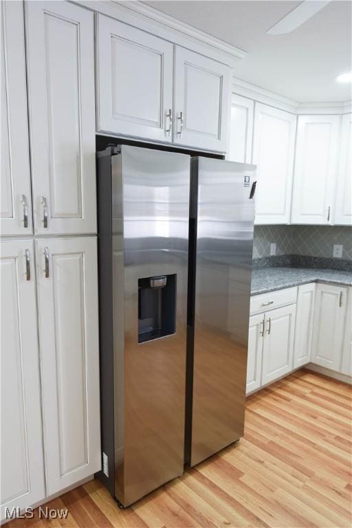 kitchen featuring white cabinets, dark stone countertops, decorative backsplash, stainless steel fridge, and light hardwood / wood-style flooring