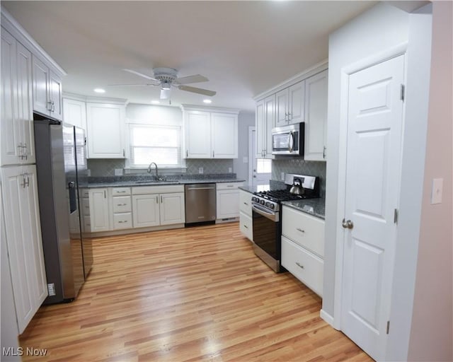 kitchen featuring appliances with stainless steel finishes, white cabinetry, decorative backsplash, light wood-type flooring, and ceiling fan