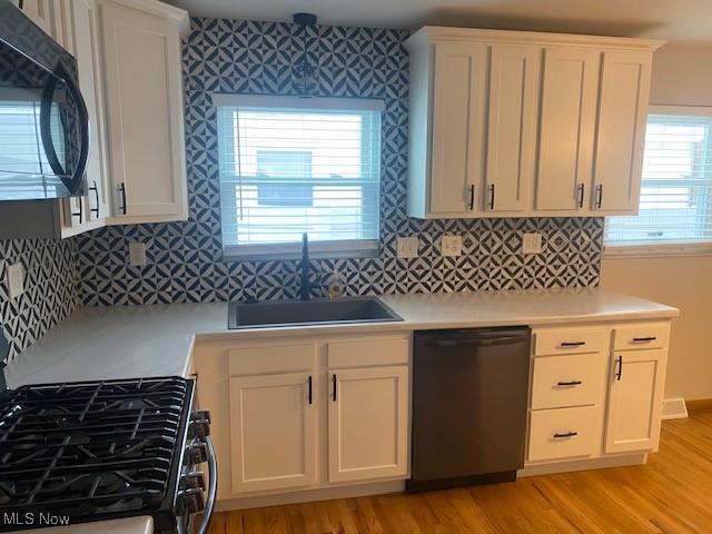 kitchen with black appliances, light wood-type flooring, white cabinets, and sink