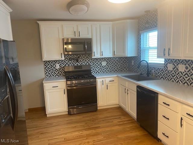 kitchen featuring sink, white cabinetry, tasteful backsplash, light hardwood / wood-style floors, and appliances with stainless steel finishes