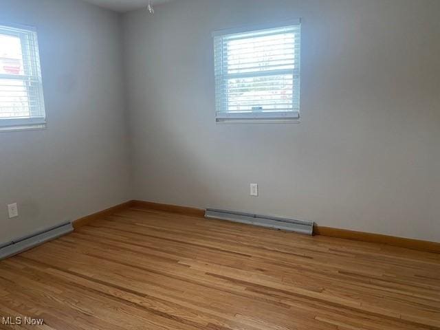 empty room with a baseboard heating unit, a wealth of natural light, and light hardwood / wood-style flooring