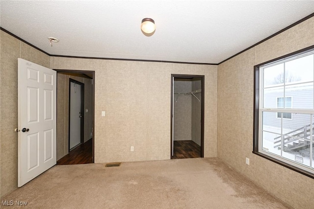 unfurnished bedroom with a textured ceiling, a spacious closet, ornamental molding, a closet, and dark colored carpet