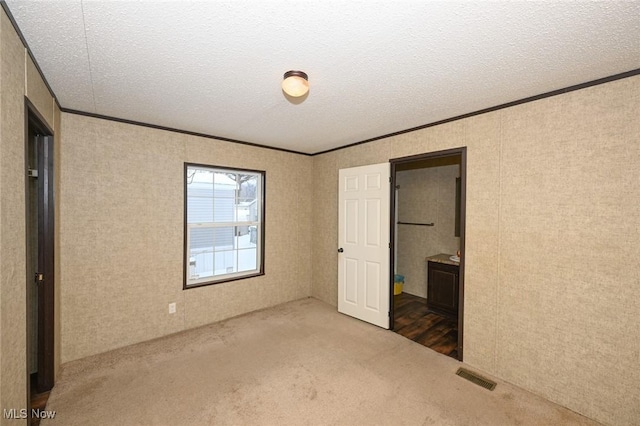 unfurnished bedroom featuring a textured ceiling, connected bathroom, carpet, and crown molding