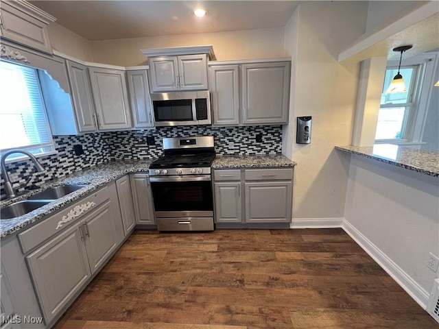 kitchen with light stone countertops, appliances with stainless steel finishes, dark hardwood / wood-style flooring, sink, and gray cabinetry