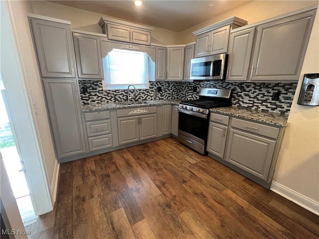 kitchen with appliances with stainless steel finishes, gray cabinetry, dark hardwood / wood-style floors, light stone counters, and sink