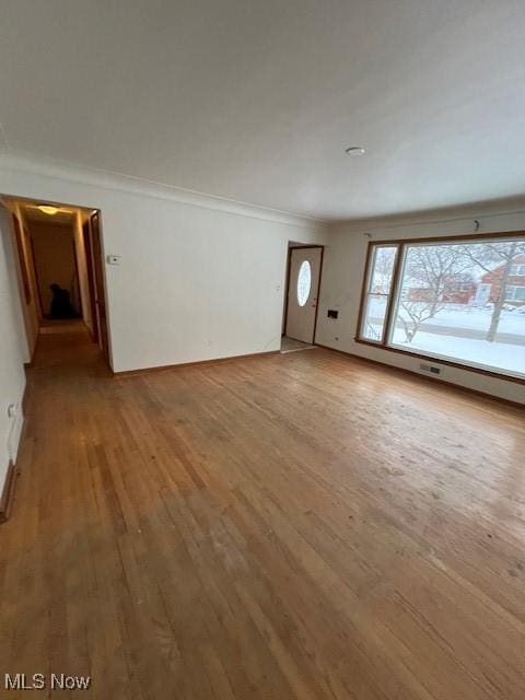 unfurnished living room featuring ornamental molding and wood-type flooring