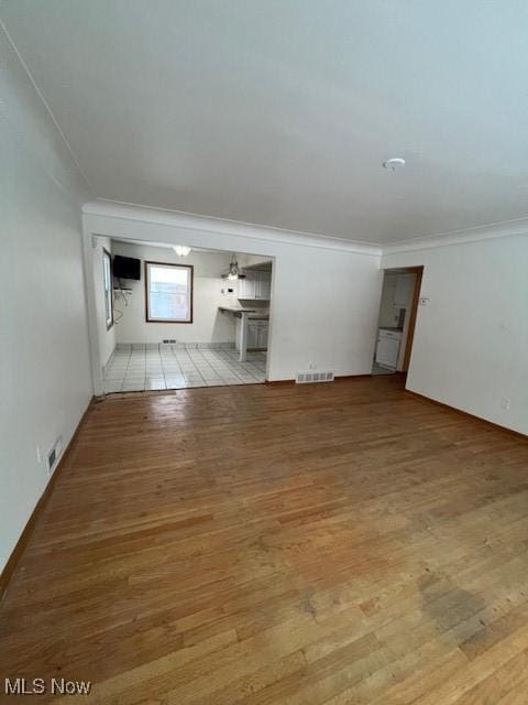 unfurnished living room with light wood-type flooring, crown molding, and a wall unit AC