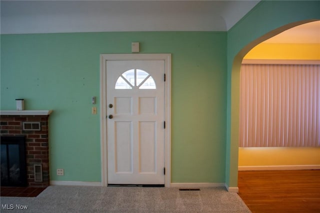 carpeted foyer entrance with a brick fireplace