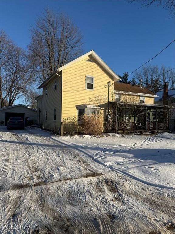 view of snow covered exterior featuring an outbuilding and a garage