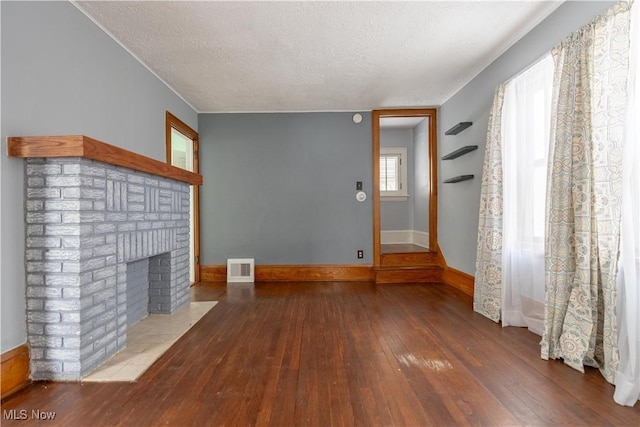 unfurnished living room with a brick fireplace, a textured ceiling, and hardwood / wood-style floors