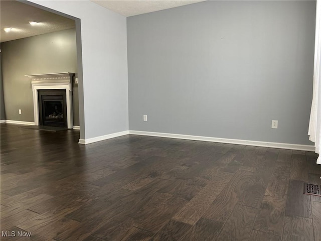 unfurnished living room featuring baseboards, a fireplace, visible vents, and dark wood-type flooring