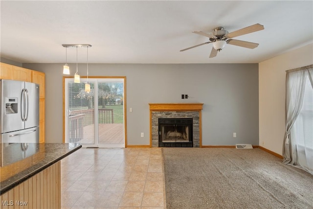 unfurnished living room featuring ceiling fan and a stone fireplace