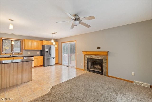 kitchen with sink, stainless steel fridge, a tile fireplace, hanging light fixtures, and light carpet