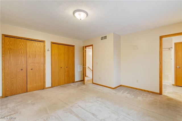 unfurnished bedroom featuring multiple closets and light carpet