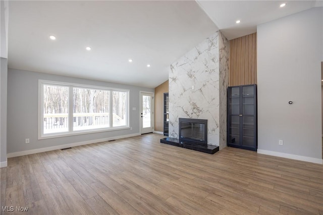 unfurnished living room with a high end fireplace, vaulted ceiling, and light hardwood / wood-style flooring