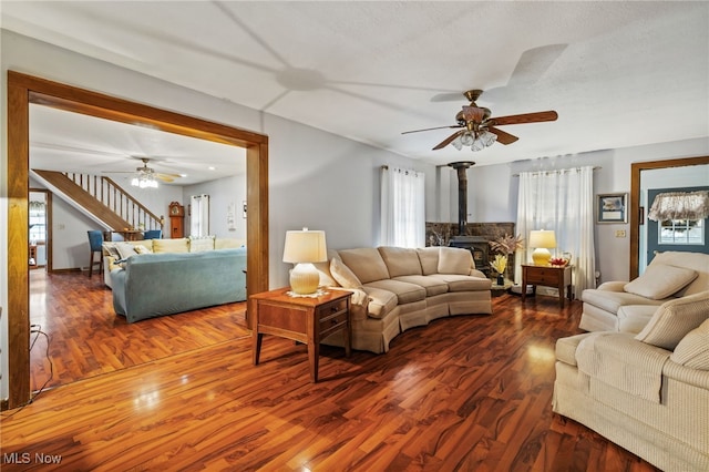 living room featuring dark wood-type flooring, a textured ceiling, ceiling fan, and a wood stove