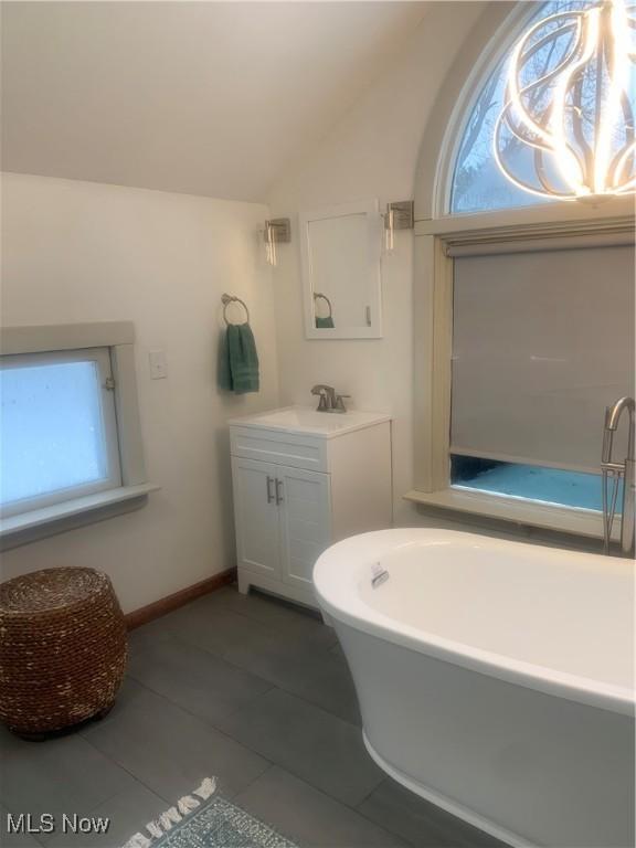 bathroom featuring lofted ceiling, vanity, tile patterned flooring, and a bath