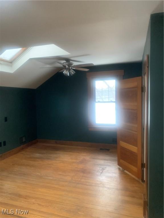 additional living space with ceiling fan, light wood-type flooring, and lofted ceiling with skylight