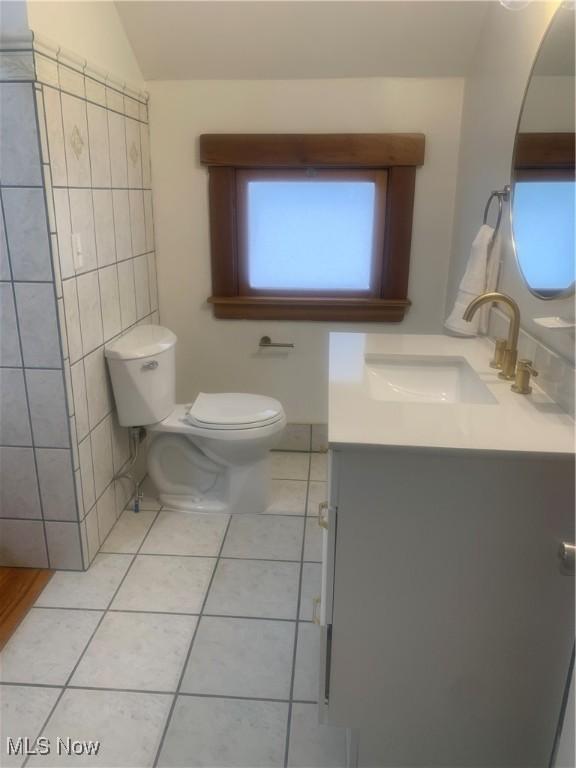 bathroom featuring vaulted ceiling, tile patterned flooring, tile walls, toilet, and vanity