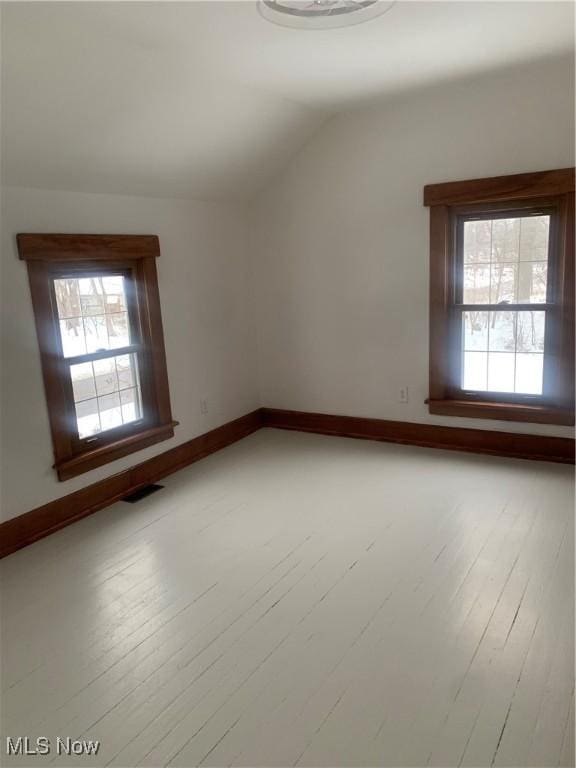 spare room with hardwood / wood-style floors, vaulted ceiling, baseboards, and visible vents
