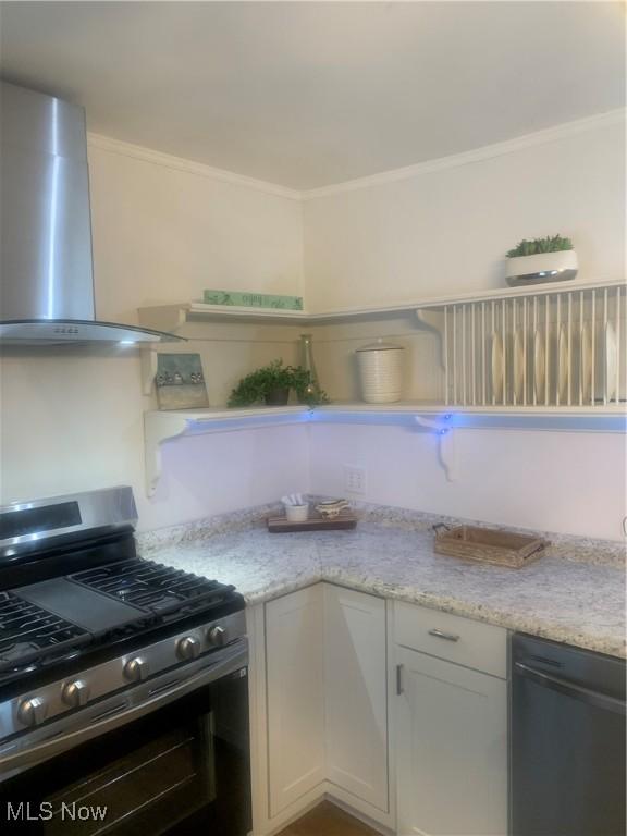 kitchen with light stone countertops, stainless steel gas range oven, wall chimney exhaust hood, black dishwasher, and white cabinetry