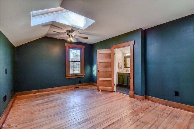 unfurnished bedroom with vaulted ceiling with skylight, light wood-style floors, baseboards, and ensuite bathroom