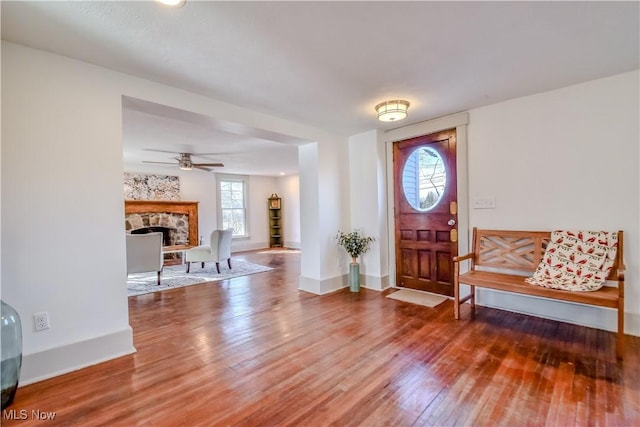 foyer entrance featuring ceiling fan, a fireplace, baseboards, and wood finished floors