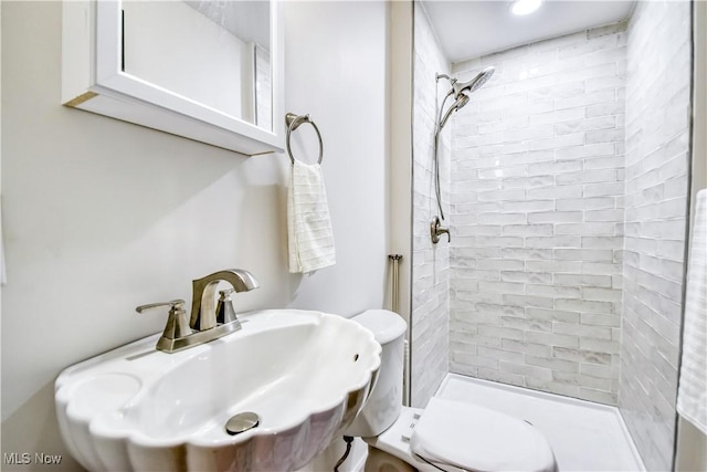 bathroom featuring toilet, tiled shower, and a sink