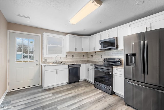 kitchen with white cabinetry, light hardwood / wood-style floors, appliances with stainless steel finishes, tasteful backsplash, and sink