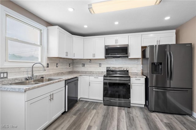 kitchen featuring stainless steel appliances, decorative backsplash, white cabinets, light hardwood / wood-style flooring, and sink