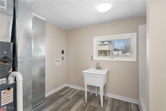 laundry room with hardwood / wood-style flooring, a textured ceiling, and heating unit