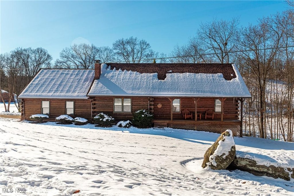 snow covered rear of property featuring covered porch