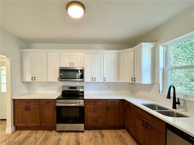 kitchen with white cabinets, sink, stainless steel appliances, and light hardwood / wood-style flooring