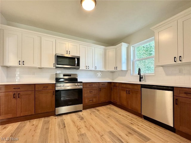 kitchen featuring decorative backsplash, sink, white cabinetry, light hardwood / wood-style flooring, and appliances with stainless steel finishes