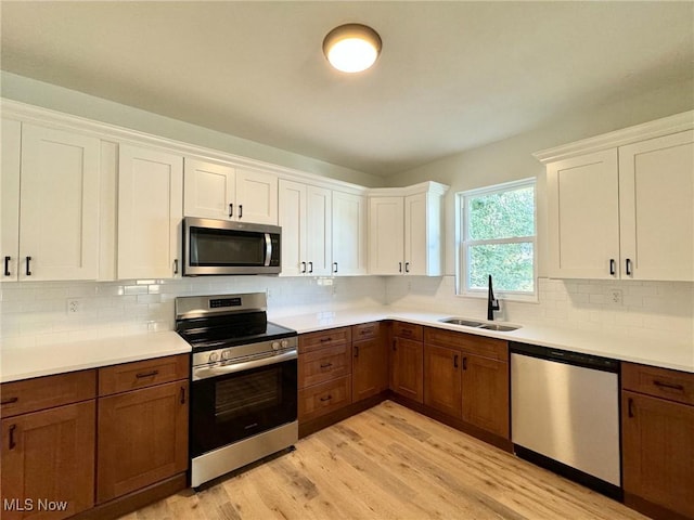 kitchen featuring appliances with stainless steel finishes, white cabinetry, tasteful backsplash, sink, and light wood-type flooring