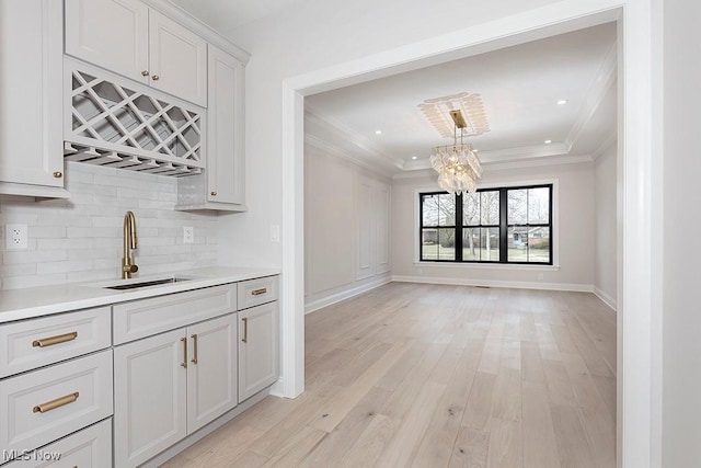 interior space featuring baseboards, ornamental molding, wet bar, light wood-type flooring, and a sink