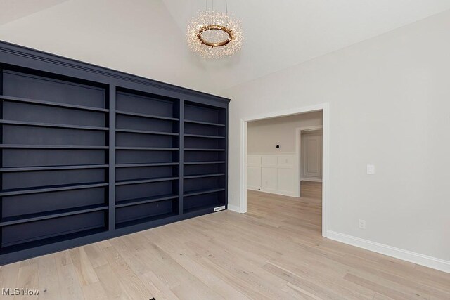 empty room with light wood-style floors, a chandelier, vaulted ceiling, and baseboards