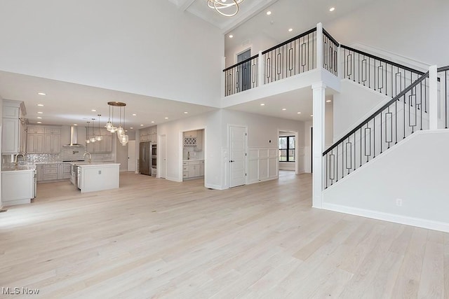 unfurnished living room with a towering ceiling, stairway, light wood finished floors, and recessed lighting