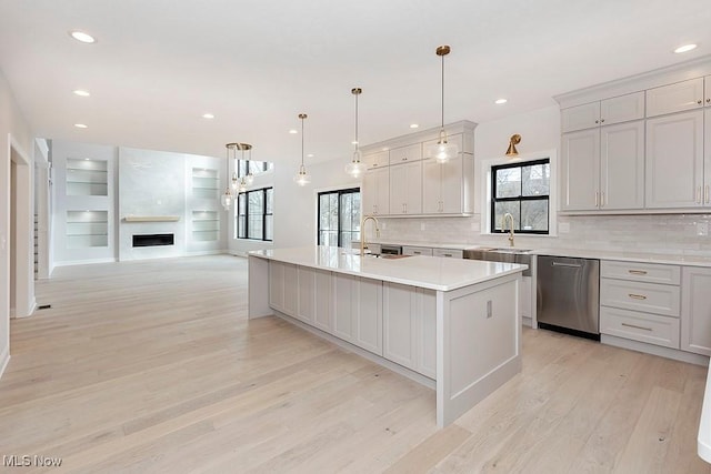 kitchen with dishwasher, an island with sink, light wood-style flooring, light countertops, and a fireplace