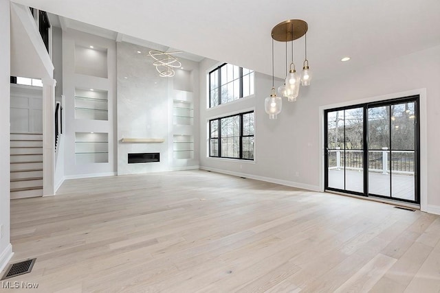 unfurnished living room featuring a large fireplace, light wood finished floors, baseboards, visible vents, and built in shelves