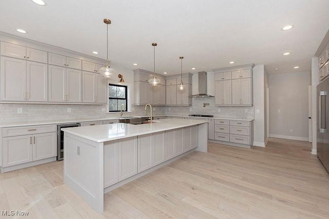 kitchen featuring beverage cooler, wall chimney exhaust hood, light wood-style flooring, light countertops, and a large island with sink