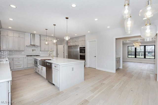 kitchen with backsplash, a sink, built in appliances, light wood-type flooring, and wall chimney exhaust hood