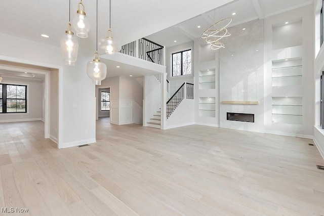 unfurnished living room with a high ceiling, wood finished floors, built in features, stairs, and a wealth of natural light